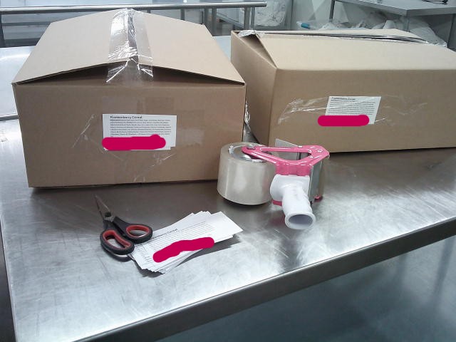 Two boxes with a tape gun, scissors, and labels.